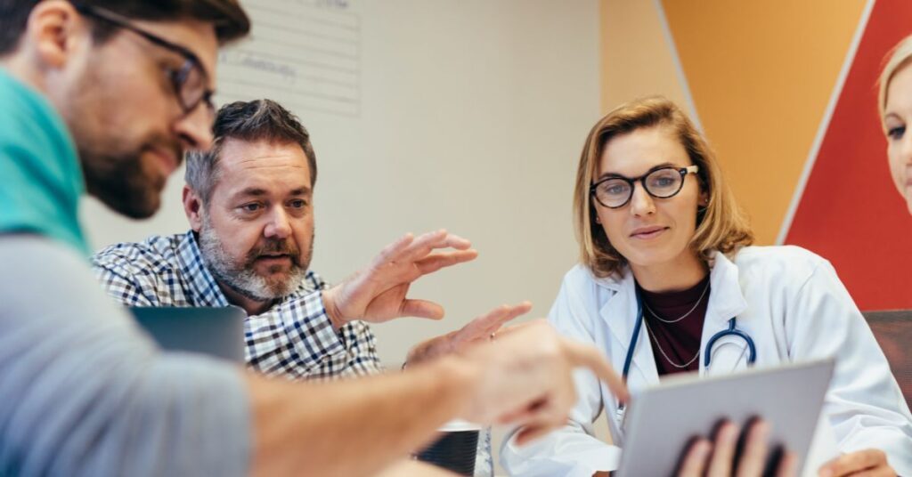 A doctor and 2 men talking over a tablet