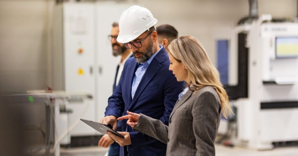 man and woman in hard hat in factory reading off a tablet device