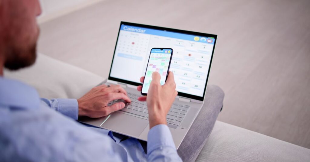 Man holding mobile and laptop both displaying online calendars