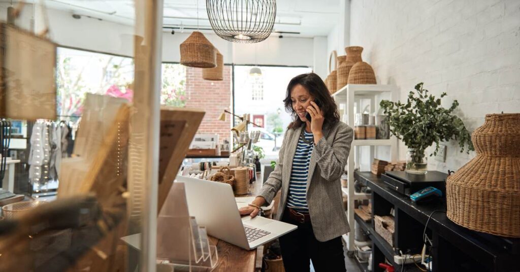 Woman on laptop on the phone in small business shop