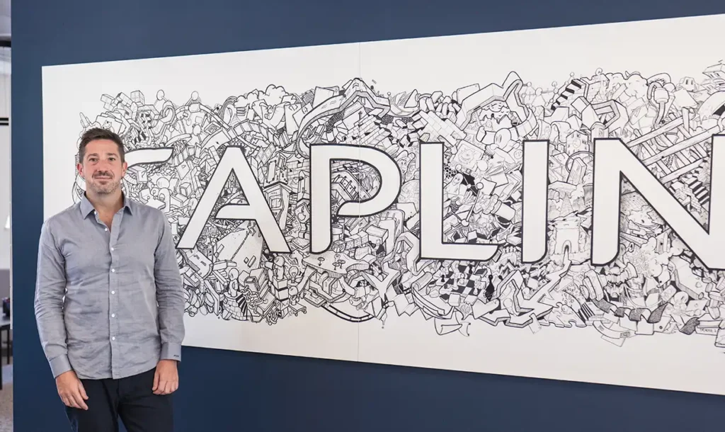 Andy Brady, Head of Customer Success at Caplin, photoed in front of the company's logo