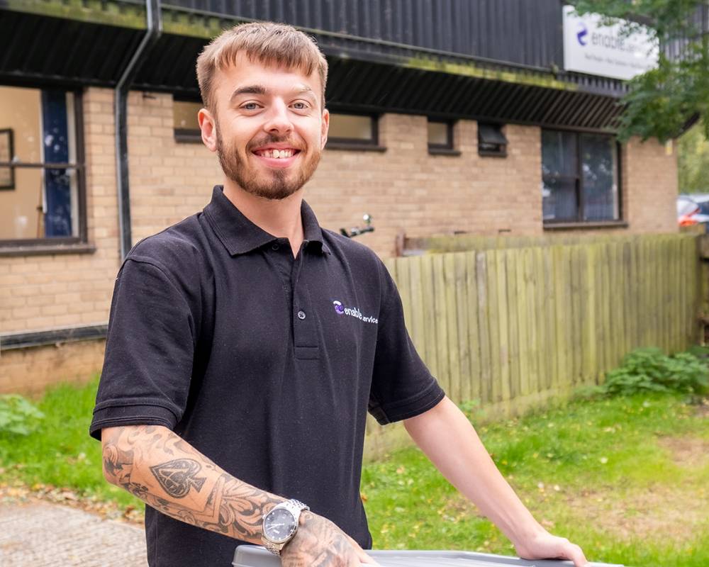 Man outside smiling at camera wearing enable.services polo shirt